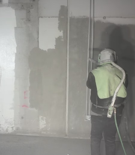 Dustless sandblasting operator removing graffiti and paint from a commercial concrete wall